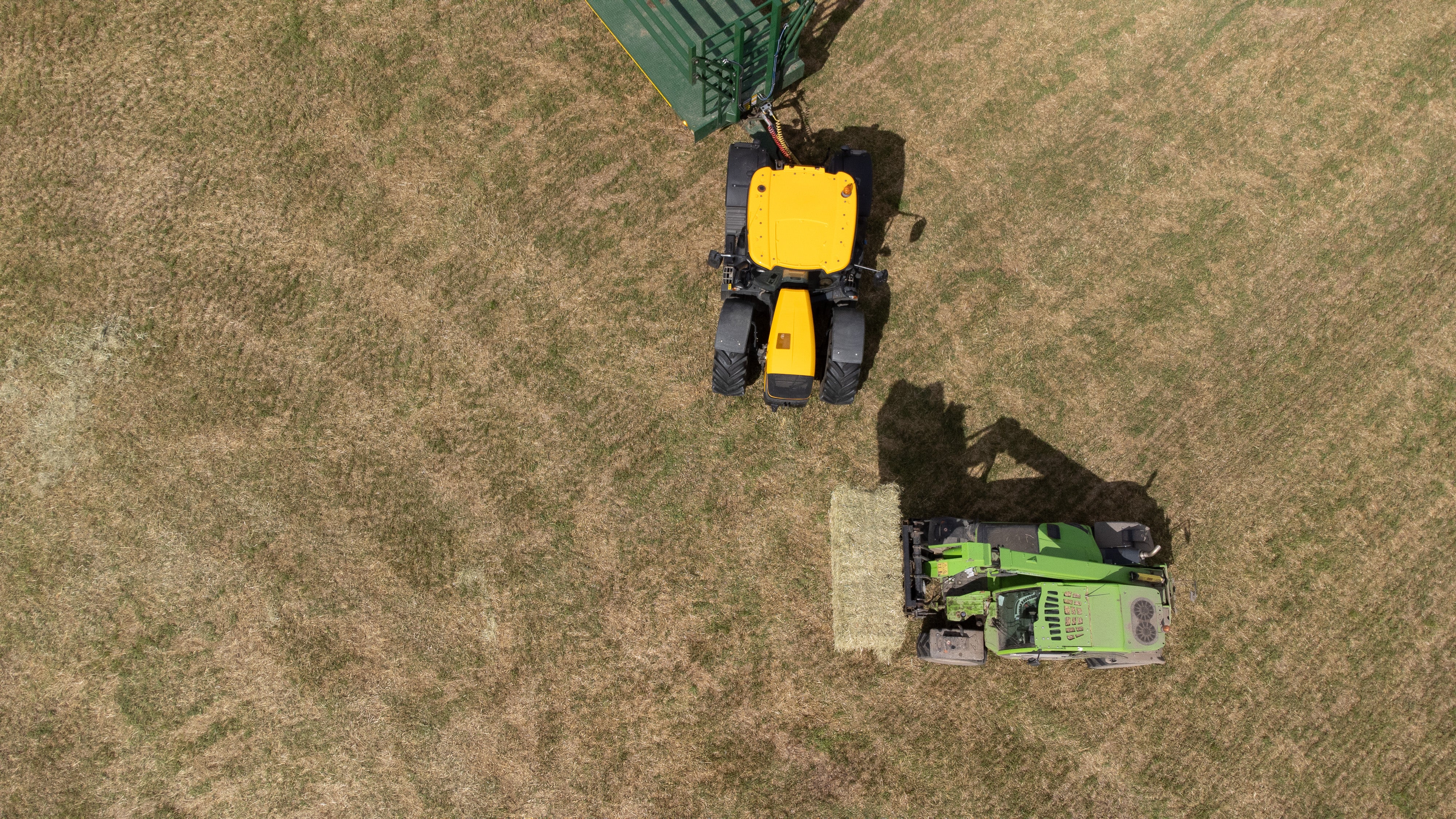 Two tractors on a grassy field, one yellow and one green, with a bale of hay.